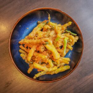 A bowl of tempura-fried potato chips sits on a wooden surface, featuring crispy, golden-brown pieces with garnish, reminiscent of a gourmet version of a bowl of chips.